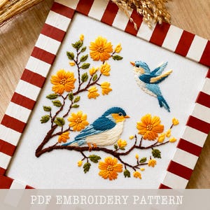 May include: Embroidered artwork showing two blue and yellow birds on a brown branch with yellow flowers. The artwork is framed in a white and red striped frame. The text "PDF EMBROIDERY PATTERN" is at the bottom.