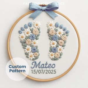May include: Embroidered baby footprints in a wooden hoop. The design features blue, cream, and white flowers arranged in the shape of feet. The name "Mateo" and the date "15/07/2025" are embroidered below the footprints. A blue ribbon bow is at the top.