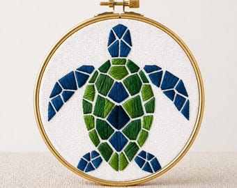 May include: Embroidered sea turtle design in shades of blue and green, set within a gold-colored hoop. The turtle is stitched on white fabric. The text "PDF EMBROIDERY PATTERN" is at the bottom.