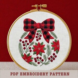 Puede incluir: Diseño de adorno navideño bordado en un aro dorado. El adorno presenta un lazo a cuadros rojo y negro, flores de pascua rojas, hojas verdes y bayas rojas. El texto "PDF EMBROIDERY PATTERN" está en la parte inferior.