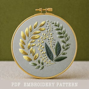 Puede incluir: Un bastidor de bordado redondo con un fondo de tela gris. El bordado presenta un diseño botánico con hilos dorados, verdes y plateados. El texto "PDF EMBROIDERY PATTERN" está en la parte inferior.