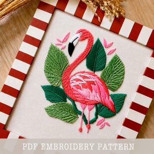 May include: Embroidered flamingo art piece with a red and white striped frame. The flamingo is pink and white, surrounded by green leaves and pink accents. The text "PDF EMBROIDERY PATTERN" is at the bottom.