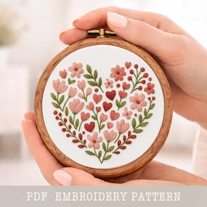 Peut inclure: Broderie en forme de cœur avec des fleurs roses, des cœurs rouges et des feuilles vertes, dans un cercle en bois. Le texte "PDF EMBROIDERY PATTERN" est en bas. L'ouvrage est tenu dans les mains.