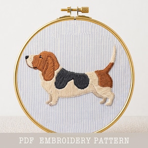 May include: An embroidery hoop with a detailed, colorful depiction of a Basset Hound. The dog is rendered in brown, black, and cream thread against a blue and white striped fabric. The text "PDF EMBROIDERY PATTERN" is at the bottom.