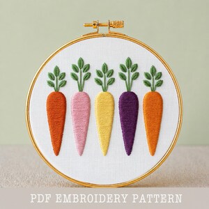 May include: A colorful embroidery hoop featuring five embroidered carrots in shades of orange, pink, yellow, purple, and orange, each with green leafy tops. The design is set against a white fabric background within a gold hoop. Text at the bottom reads "PDF EMBROIDERY PATTERN".