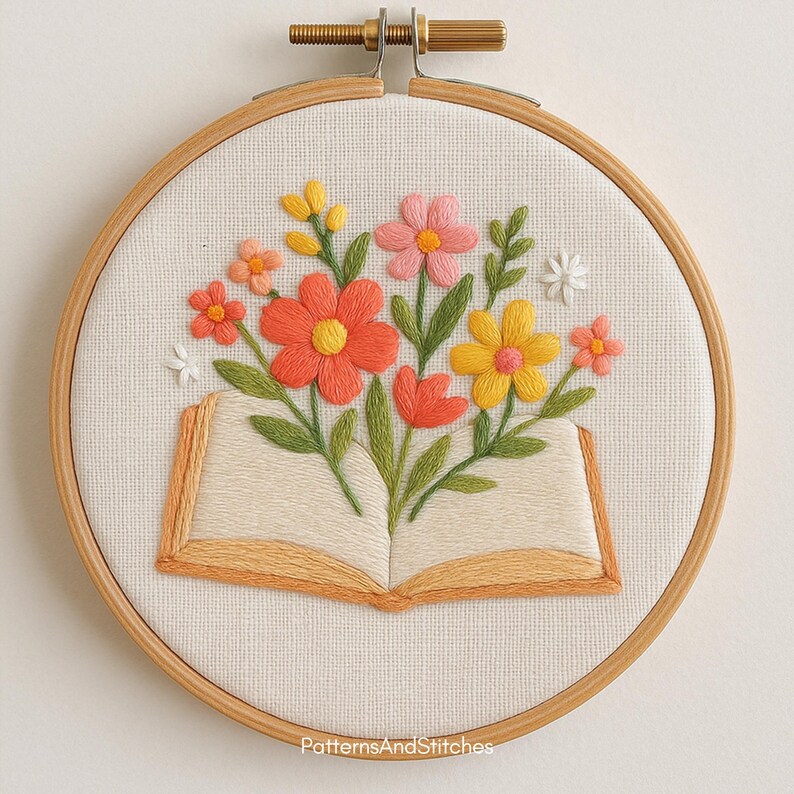 Puede incluir: Dise&ntilde;o floral bordado en un aro de madera. La obra presenta un colorido ramo de flores que emerge de un libro abierto. Las flores son en tonos naranja, rosa y amarillo, con hojas verdes. El texto "PatternsAndStitches" est&aacute; en la parte inferior.
