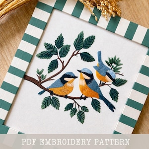 Peut inclure: Broderie représentant trois oiseaux bleus, jaunes et noirs perchés sur une branche brune avec des feuilles vertes. L'œuvre est encadrée dans un cadre en bois à rayures blanches et vertes. Le texte "PDF EMBROIDERY PATTERN" est en bas.