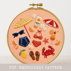May include: A round wooden embroidery hoop containing peach fabric with stitched summer motifs including a yellow striped umbrella, sunscreen bottle, red and white polka dot bikini, blue sunglasses, a crab, flip-flops, and a cocktail.
