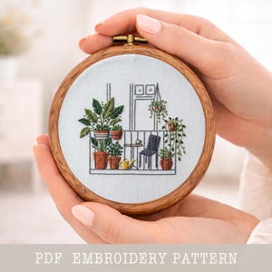 May include: A hand-held embroidery hoop featuring a detailed stitched design of a balcony with potted plants, a small table, and a chair. The embroidery is set against a light fabric, framed by a wooden hoop. The text "PDF EMBROIDERY PATTERN" is at the bottom.