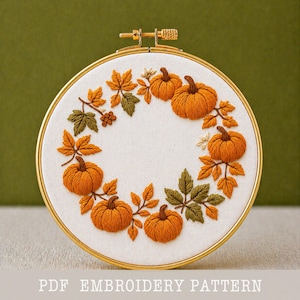 May include: A circular embroidery hoop featuring a fall-themed design. The design includes orange pumpkins and autumn leaves in shades of orange, green, and brown, arranged in a wreath pattern. The text "PDF EMBROIDERY PATTERN" is at the bottom.