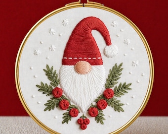 May include: Embroidered Christmas gnome design in a gold hoop. The gnome wears a red hat and has a white beard, with red roses and green leaves. The text "PDF EMBROIDERY PATTERN" is at the bottom. The embroidery is on a white fabric.