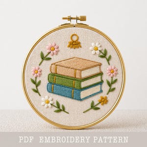 Può includere: Ricamo su telaio raffigurante una pila di tre libri marroni, verdi e blu, circondata da fiori rosa e bianchi con foglie verdi. Il disegno è ambientato su uno sfondo di tessuto beige all'interno di un telaio dorato. Il testo in basso recita "PDF EMBROIDERY PATTERN".