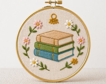 Könnte beinhalten: Gesticktes Stickrahmen-Kunstwerk mit einem Stapel von drei Büchern in Braun-, Grün- und Blautönen, umgeben von rosa und weißen Blumen mit grünen Blättern. Das Design befindet sich auf einem beigefarbenen Stoffhintergrund in einem goldenen Reifen. Der Text unten lautet "PDF EMBROIDERY PATTERN".