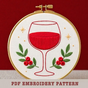 Puede incluir: Diseño de copa de vino bordada en un aro dorado. La copa está rellena de hilo rojo, rodeada de hojas verdes, bayas rojas y detalles de estrellas doradas. El texto "PDF EMBROIDERY PATTERN" está en la parte inferior.