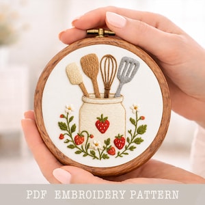 May include: A circular wooden embroidery hoop featuring a kitchen-themed design. The white fabric displays a jar with embroidered utensils and strawberries. The text "PDF EMBROIDERY PATTERN" is at the bottom of the image.