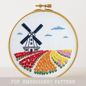 May include: A circular gold embroidery hoop containing white fabric with a hand-stitched design of a dark blue windmill set against a field of red, orange, yellow, and pink tulips under small blue clouds. The text PDF EMBROIDERY PATTERN is visible.
