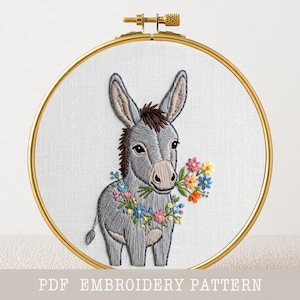 May include: A gold-coloured embroidery hoop holding a hand-stitched image of a grey donkey with a floral garland. The donkey holds a bouquet of colourful flowers. The text "PDF EMBROIDERY PATTERN" is at the bottom of the image.