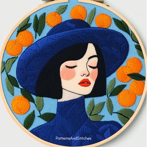 May include: Embroidered hoop art featuring a woman in a blue hat and sweater, with closed eyes and red lips. The design includes orange fruit and green leaves against a light blue background. The text "PatternsAndStitches" is at the bottom.