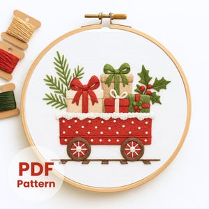 May include: Embroidered Christmas scene in a wooden hoop. A red train car with white polka dots carries wrapped gifts with green and red bows, holly, and pine branches. The text "PDF Pattern" is in the lower left corner. Spools of thread are in the upper left.