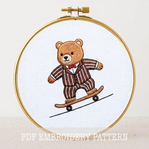 May include: Embroidered image of a brown teddy bear in a pinstripe suit and red bow tie, skateboarding on a black line. The embroidery is set in a gold hoop against a white background. Text at the bottom reads "PDF EMBROIDERY PATTERN".