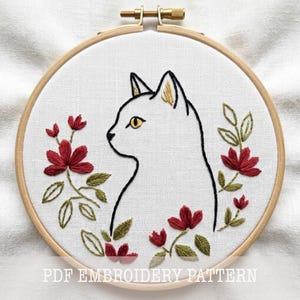 May include: Embroidery hoop featuring a white cat profile with yellow eyes and ears, surrounded by red flowers and green leaves. The text "PDF EMBROIDERY PATTERN" is at the bottom. The design is on white fabric, set in a wooden hoop.