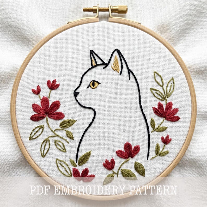 May include: Embroidery hoop featuring a white cat profile with yellow eyes and ears, surrounded by red flowers and green leaves. The text "PDF EMBROIDERY PATTERN" is at the bottom. The design is on white fabric, set in a wooden hoop.