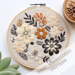 Pode incluir: Um padrão de bordado à mão com um design floral com flores pretas, brancas, bege e marrons sobre um fundo cinza. O padrão é emoldurado em um aro de madeira. O texto "HAND EMBROIDERY PATTERN" é visível no canto inferior direito.