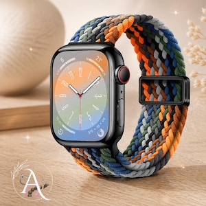 May include: A black smartwatch with a colorful braided band in shades of orange, blue, green, and gray. The watch face displays the time. The band is secured with a black metal clasp. The watch is on a wooden surface.