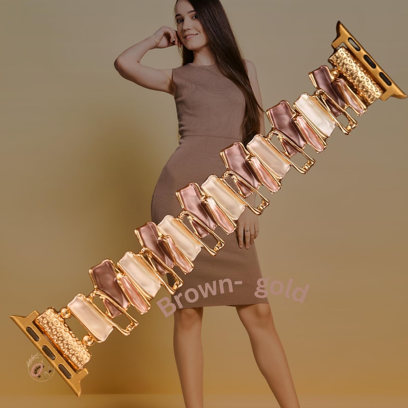 May include: Gold-tone Apple Watch band with a multi-colored, geometric design. The band features a series of interlocking, rectangular shapes in shades of pink, white, and gold.