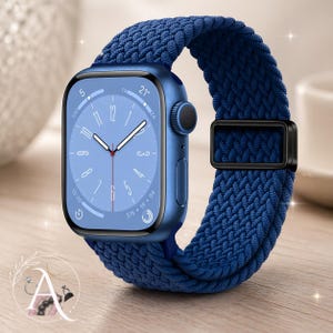 May include: A blue smartwatch with a matching woven band. The watch face displays the time and other information. The band is secured with a black metal clasp. The watch is on a light-colored surface.