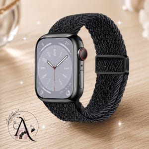 May include: A black smartwatch with a braided black band. The watch face displays the time and other metrics. The watch has a black case with a red button. The band is secured with a black buckle. The watch is on a wooden surface.