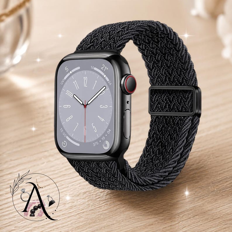 May include: A black smartwatch with a braided black band. The watch face displays the time and other metrics. The watch has a black case with a red button. The band is secured with a black buckle. The watch is on a wooden surface.