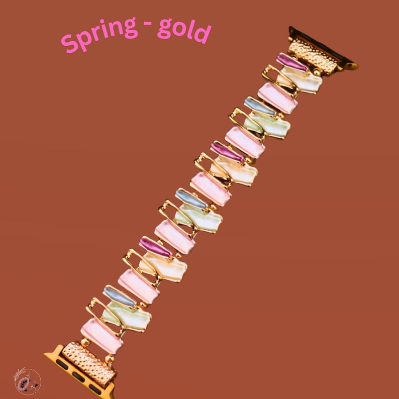 May include: A gold-toned watch band with a colorful geometric design. The band is made of metal and has a spring-like appearance. The band is designed to fit a smartwatch.