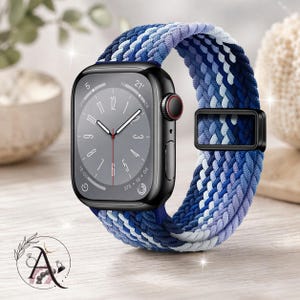 May include: A black smartwatch with a gray face and a braided watch band. The band features a mix of blue, white, and purple hues. The watch has a black buckle and a red dial. The watch is displayed on a wooden surface.