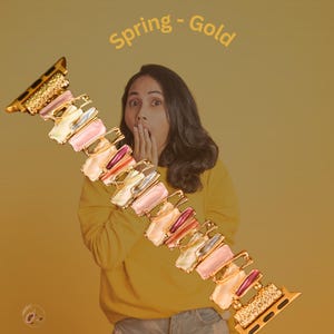 May include: A gold and multi-colored watch band with a spring-like design. The band is made of metal and has a variety of colored stones. The text "Spring - Gold" is written above the band.