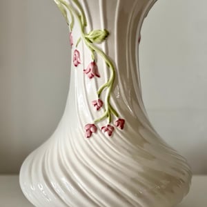 May include: White ceramic vase with a swirling design and floral accents. The vase has a delicate floral pattern with pink and green flowers.