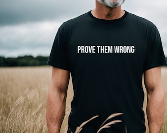 May include: A man wearing a black t-shirt with the text "PROVE THEM WRONG" in white lettering. He is standing in a field of tall grass.