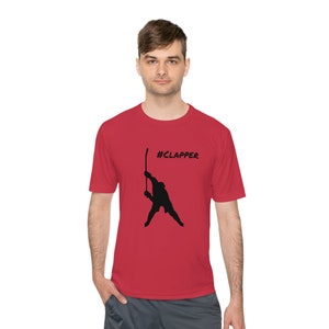 May include: Red t-shirt with a black silhouette of a hockey player holding a stick and the text "#CLAPPER" printed on the front.