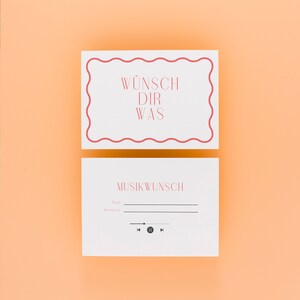 Könnte beinhalten: Zwei weiße Karten mit rotem Text und Rändern auf orangefarbenem Hintergrund. Auf der oberen Karte steht "WÜNSCH DIR WAS" in einer dekorativen Schriftart. Auf der unteren Karte steht "MUSIKWUNSCH" mit Zeilen für "Titel" und "Interpret" und einem Musikplayer-Symbol.