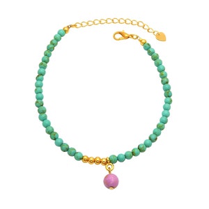 Könnte beinhalten: Ein goldfarbenes Armband mit türkisfarbenen Perlen und goldenen Akzenten. Ein rosa, runder Anhänger hängt in der Mitte. Das Armband hat eine verstellbare Kette und einen herzförmigen Anhänger am Ende.