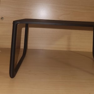 May include: A black metal shelf with a rectangular top and curved legs. The shelf is designed to be placed inside a cabinet or closet for additional storage. The shelf is made of metal and has a matte finish.