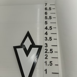 Könnte beinhalten: Ein weißes und schwarzes geometrisches Design mit einem Lineal, das Messungen in Zentimetern anzeigt. Das Design ist eine stilisierte Pfeilform mit weißem Innenraum und schwarzem Umriss. Das Lineal ist von 1,3 cm bis 17,8 cm markiert.