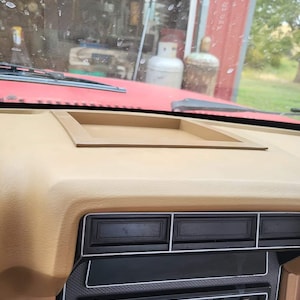 May include: A tan dashboard with a black radio and a beige tray on top. The radio has a volume knob, a tune knob, and a cassette player. The tray is rectangular and has a raised edge.