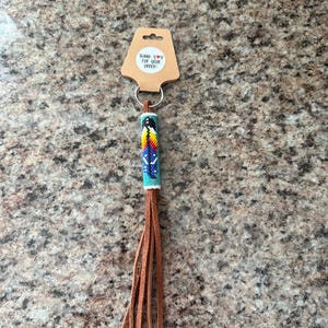 May include: A beaded keychain with a colorful design and a brown leather tassel. The beaded section features blue, yellow, red, and black beads. The keychain includes a tag that says "THANK YOU FOR YOUR ORDER!"