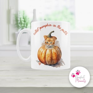 May include: White ceramic mug featuring a watercolour illustration of an orange cat inside a pumpkin. The text "cutest pumpkin in the patch" is written in orange on the mug.