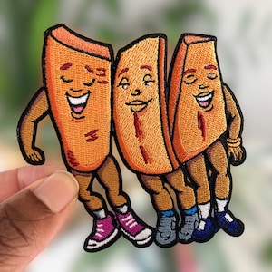 May include: Three embroidered patches of cartoon sweet potato fries wearing shoes and smiling. The fries are orange and brown with red accents.