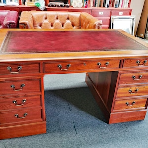 May include: A large, dark wood desk with a red leather top and multiple drawers. The desk has a traditional design with brass hardware.