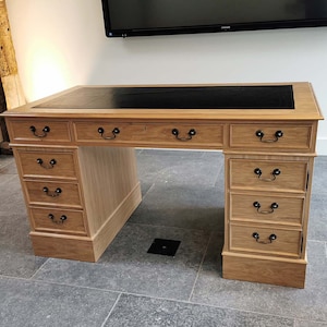 May include: A large wooden desk with a black leather top and multiple drawers. The desk has a traditional style with ornate details and black metal drawer pulls.