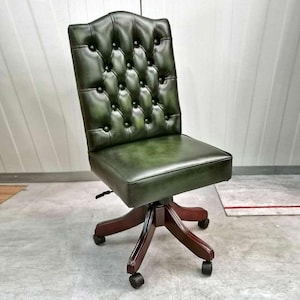 Peut inclure: Un fauteuil de bureau en cuir vert avec un dossier capitonné et une base pivotante. Le fauteuil a une structure en bois foncé et cinq roulettes.