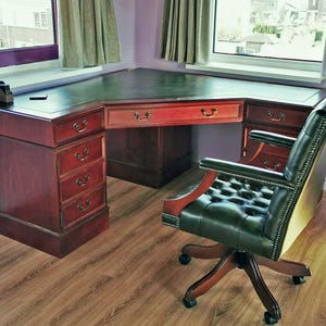 Può includere: Una scrivania ad angolo in legno scuro con un piano in pelle verde e cinque cassetti. Una sedia da ufficio in pelle nera con imbottitura a bottoni si trova di fronte alla scrivania.